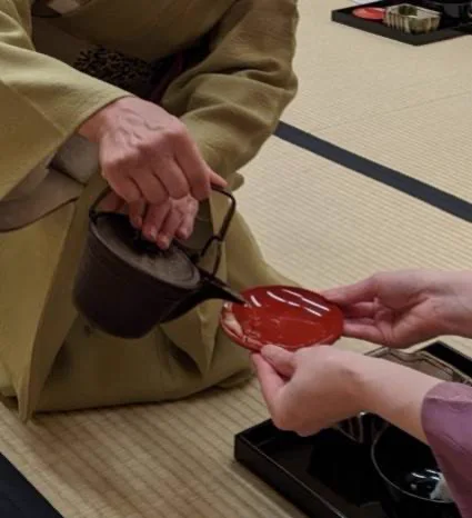 急須から赤い盃にお茶を注ぐ手元